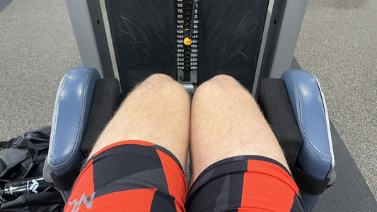 Seat-down view on a hip abduction machine: black CHCK3D Cushie Pads strapped inside both leg pads with Anchor Bands, knees close together at the deep-stretch start